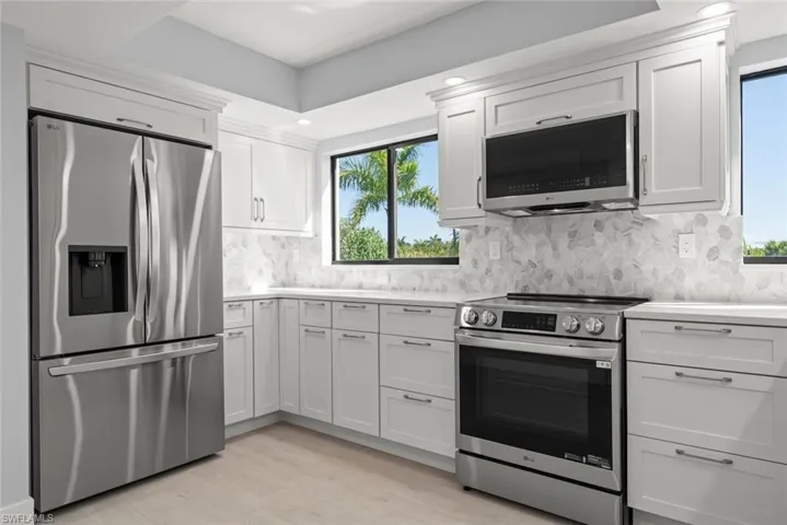 Kitchen featuring stainless steel appliances, light wood-style flooring, white cabinetry, and light stone countertops