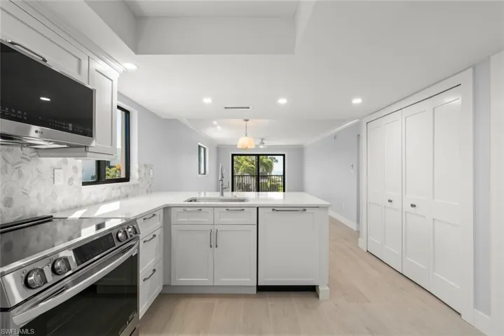 Kitchen with stainless steel appliances, a peninsula, white cabinetry, light stone countertops, and ornamental molding