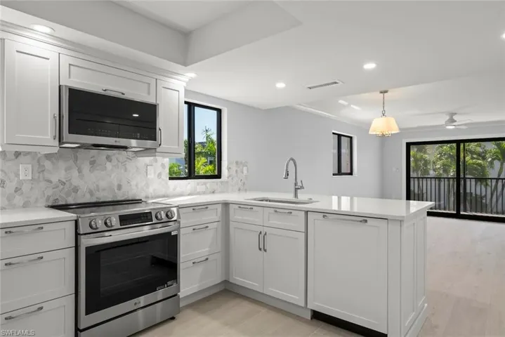 Kitchen featuring stainless steel appliances, backsplash, light stone countertops, a peninsula, and a ceiling fan