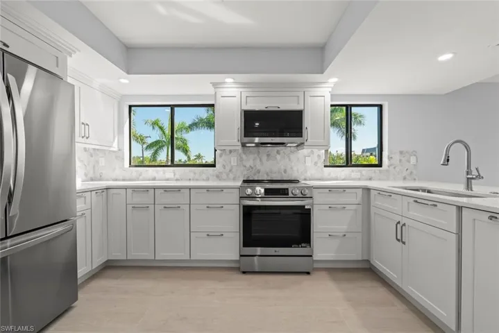 Kitchen featuring stainless steel appliances, tasteful backsplash, light stone counters, white cabinets, and recessed lighting