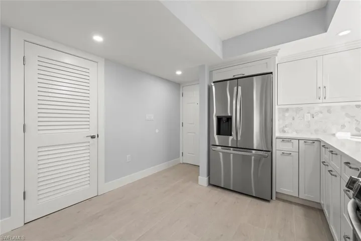 Kitchen featuring stainless steel fridge, recessed lighting, light stone counters, white cabinets, and black range