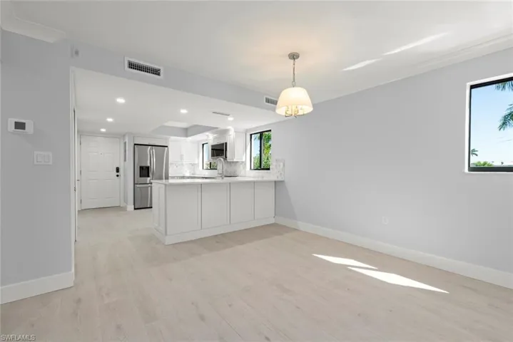 Kitchen featuring a peninsula, stainless steel appliances, white cabinetry, light wood-style flooring, and decorative light fixtures