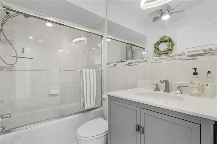 Full bathroom with tile walls, combined bath / shower with glass door and ceiling fan.
