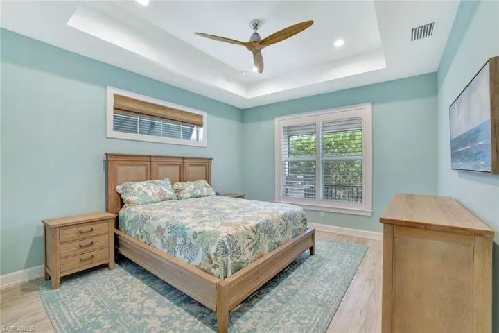 Bedroom with a raised ceiling, baseboards, visible vents, and light wood-type flooring