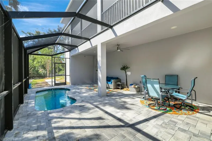 View of pool with glass enclosure, outdoor dining space, a ceiling fan, and a patio area