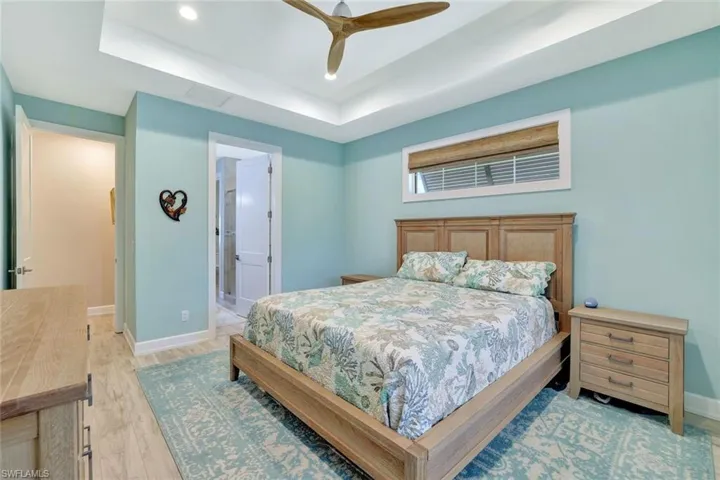 Bedroom with a raised ceiling, a ceiling fan, recessed lighting, light wood-style floors, and baseboards