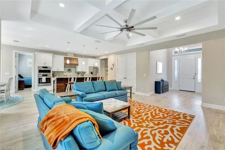 Living room featuring visible vents, baseboards, light wood-type flooring, ceiling fan with notable chandelier, and coffered ceiling