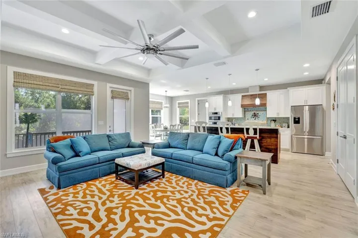 Living area with visible vents, a ceiling fan, coffered ceiling, light wood-style floors, and baseboards