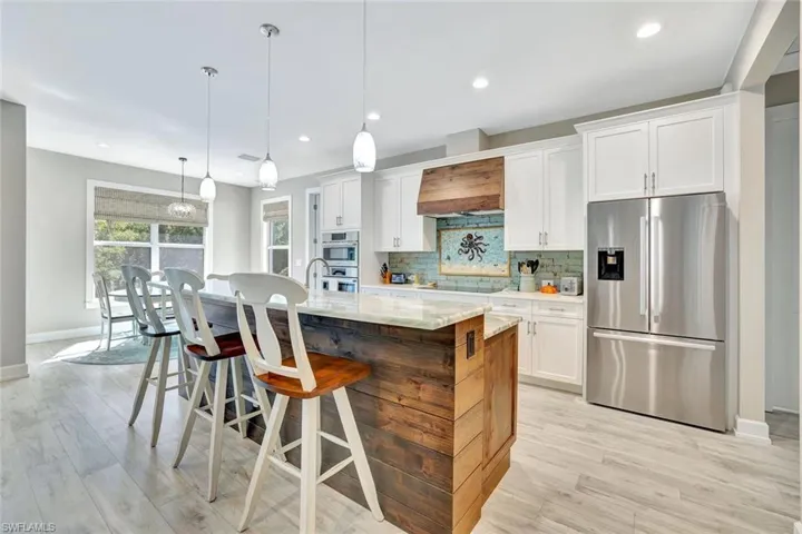 Kitchen with backsplash, premium range hood, a center island with sink, appliances with stainless steel finishes, and white cabinetry