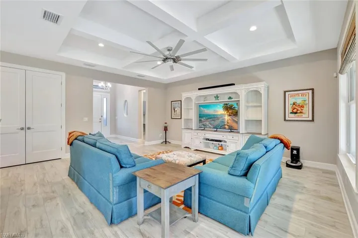Living room featuring light wood-type flooring, visible vents, coffered ceiling, and a ceiling fan