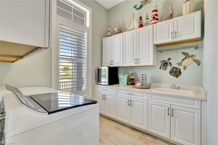 Kitchen featuring white cabinetry, washing machine and clothes dryer, light wood-style floors, and a sink