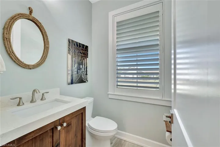 Half bath with toilet, vanity, baseboards, and wood finished floors