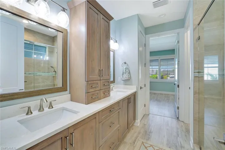 Bathroom with a tile shower, visible vents, double vanity, and a sink