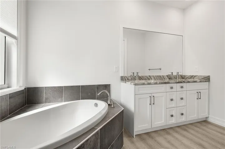Bathroom with a relaxing tiled tub, vanity, and hardwood / wood-style flooring