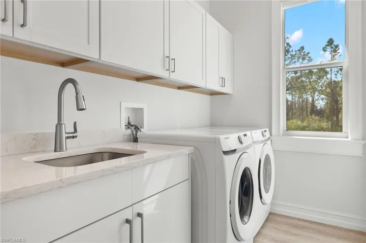 Clothes washing area featuring light wood-type flooring, washer and dryer, sink, and cabinets