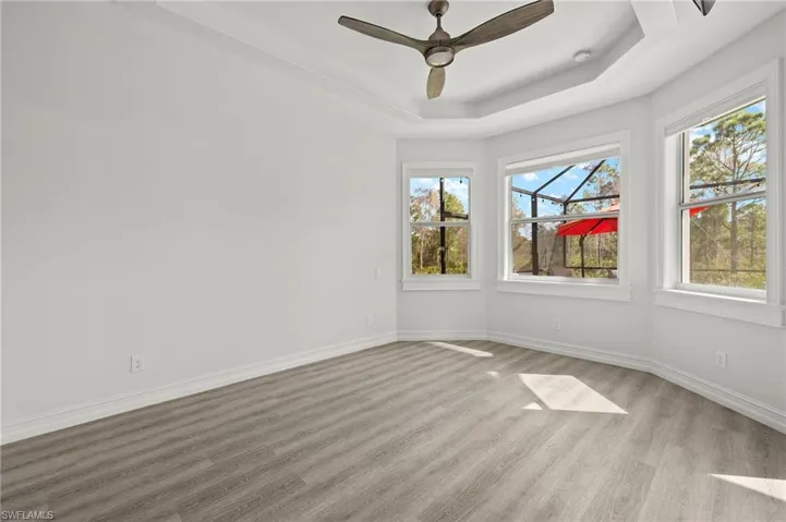 Empty room featuring ceiling fan, light wood-type flooring, and a tray ceiling