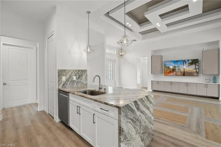 Kitchen featuring light stone counters, hanging light fixtures, stainless steel dishwasher, white cabinetry, and light hardwood / wood-style floors