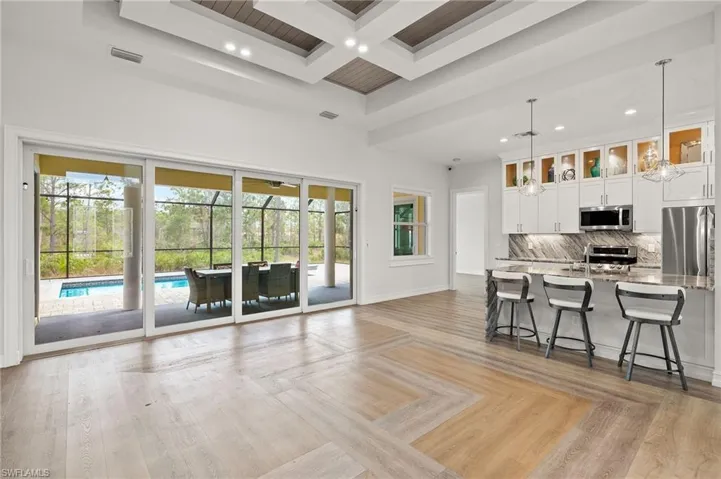 Kitchen with light stone counters, white cabinets, hanging light fixtures, beam ceiling, and appliances with stainless steel finishes