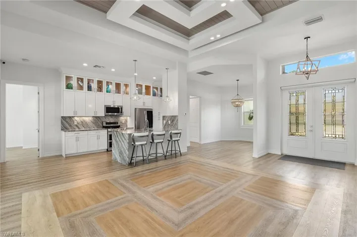 Kitchen with white cabinets, light hardwood / wood-style floors, pendant lighting, appliances with stainless steel finishes, and backsplash