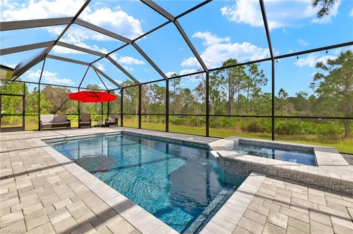 View of pool with an in ground hot tub, glass enclosure, and a patio area