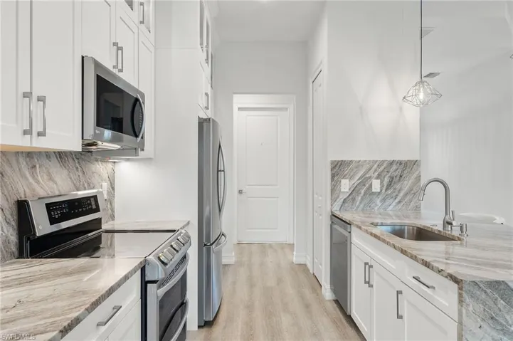 Kitchen featuring decorative light fixtures, stainless steel appliances, sink, and white cabinetry
