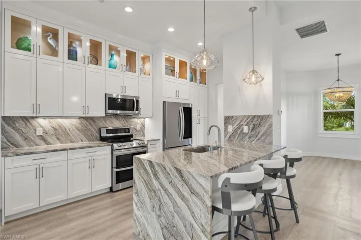 Kitchen featuring appliances with stainless steel finishes, pendant lighting, light stone countertops, and white cabinetry
