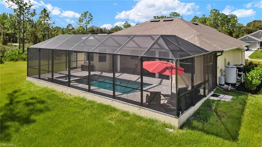 Back of property with a yard, a pool with hot tub, glass enclosure, and a patio area