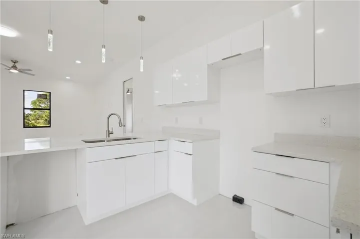 Kitchen with white cabinetry, modern cabinets, light stone countertops, decorative light fixtures, and a peninsula