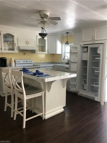 Kitchen with dark hardwood / wood-style flooring, stove, fridge, a breakfast bar, and white cabinets