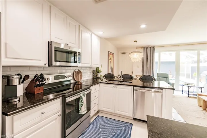 Kitchen with white cabinetry, light tile patterned floors, kitchen peninsula, backsplash, and stainless steel appliances