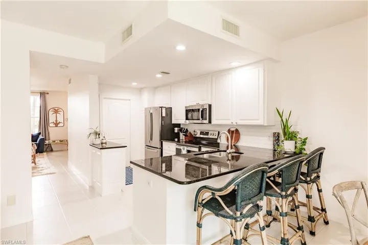 Kitchen featuring white cabinetry, stainless steel appliances, kitchen peninsula, sink, and light tile patterned floors