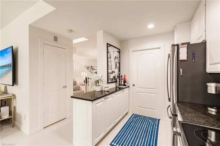 Kitchen with kitchen peninsula, white cabinets, dark stone countertops, stove, and light tile patterned floors