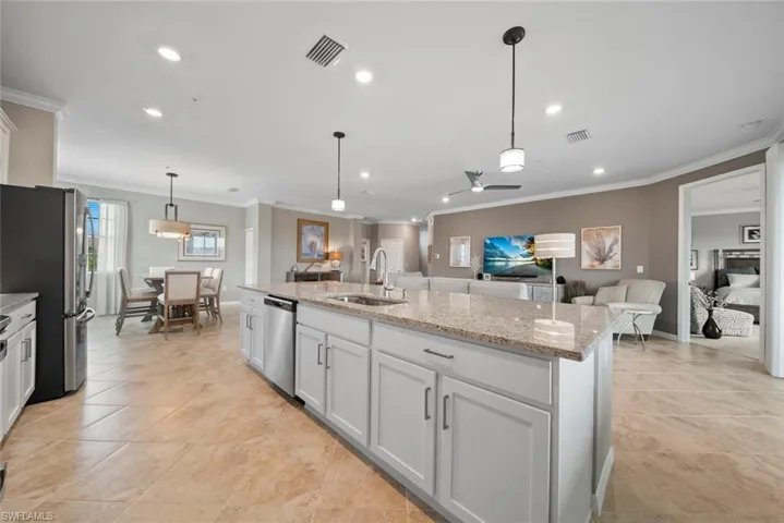 Kitchen with appliances with stainless steel finishes, sink, hanging light fixtures, white cabinetry, and a center island with sink