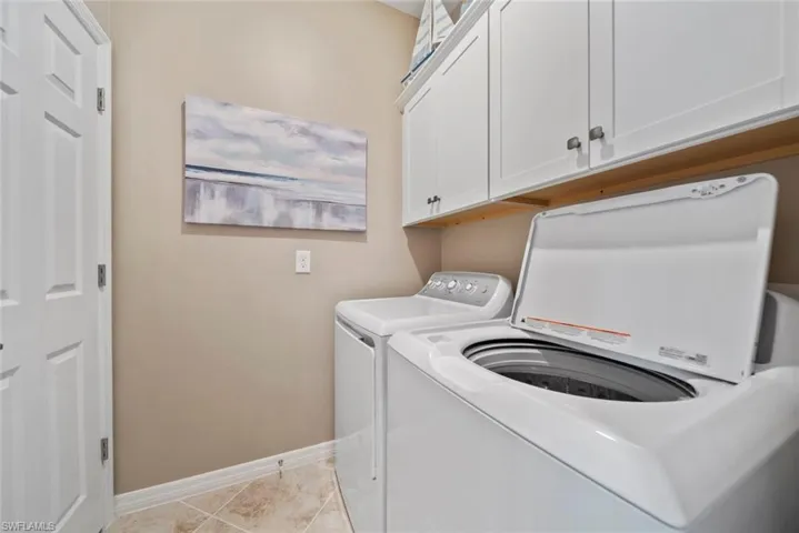 Laundry area with washer and clothes dryer, light tile patterned floors, and cabinets