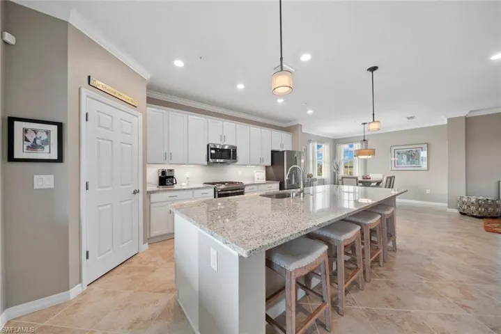 Kitchen with a center island with sink, appliances with stainless steel finishes, white cabinetry, pendant lighting, and light stone counters