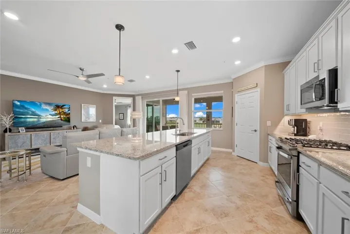 Kitchen with appliances with stainless steel finishes, white cabinets, backsplash, and an island with sink