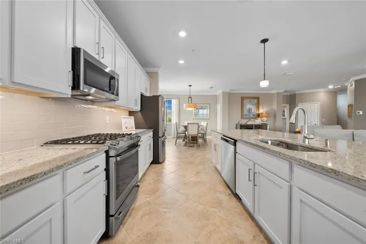 Kitchen with stainless steel appliances, ornamental molding, sink, pendant lighting, and white cabinetry