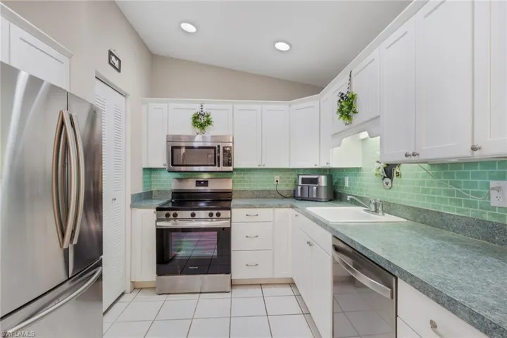 Kitchen with stainless steel appliances, white cabinets, vaulted ceiling, decorative backsplash, and light tile patterned floors