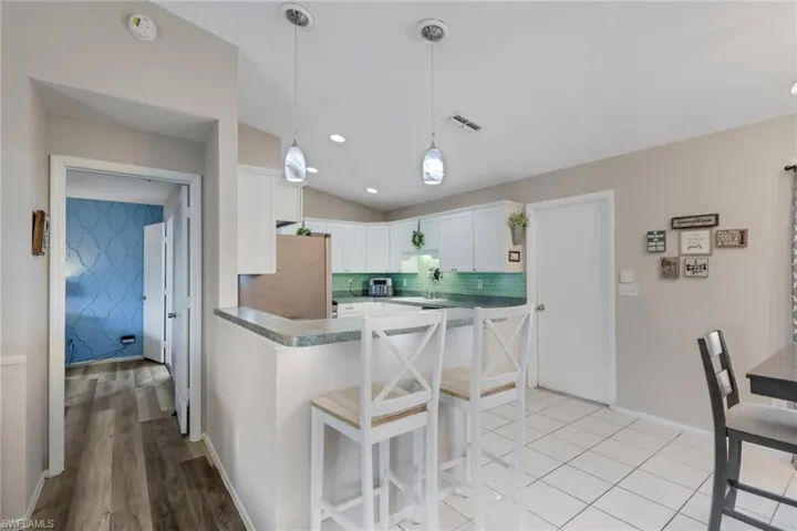 Kitchen with a kitchen breakfast bar, decorative light fixtures, vaulted ceiling, white cabinetry, and a peninsula