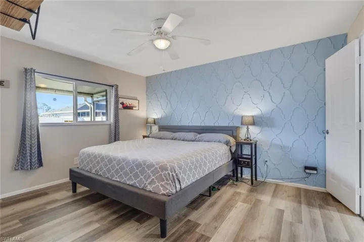 Bedroom featuring wallpapered walls, an accent wall, light wood-type flooring, and a ceiling fan