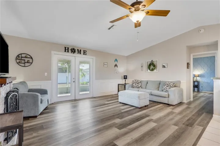 Living room with french doors, a ceiling fan, lofted ceiling, light wood-type flooring, and wainscoting
