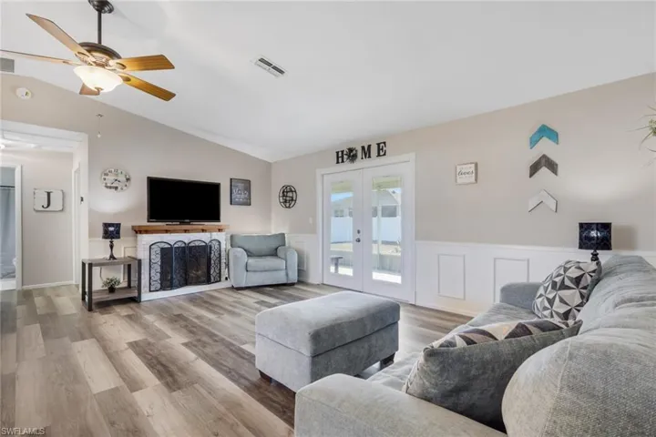 Living room featuring wood finished floors, a ceiling fan, french doors, lofted ceiling, and a wainscoted wall