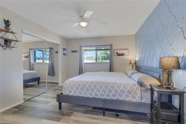 Bedroom with wood finished floors, an accent wall, a ceiling fan, a closet, and wallpapered walls
