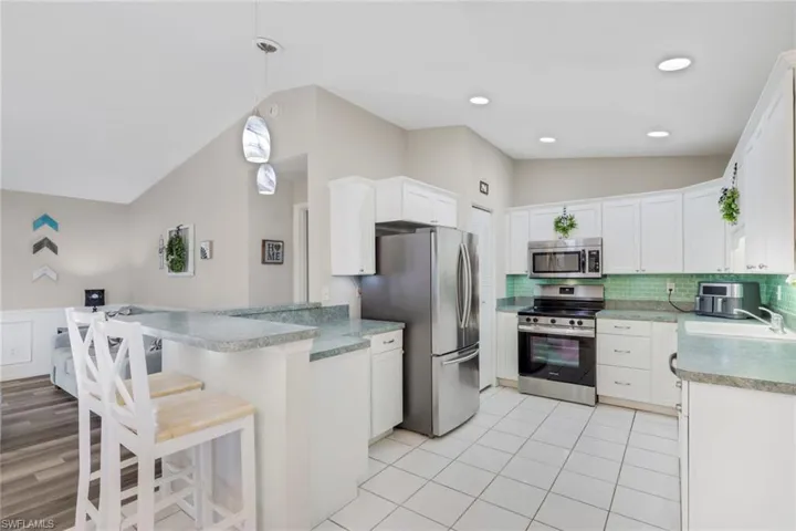 Kitchen featuring vaulted ceiling, a breakfast bar, stainless steel appliances, decorative light fixtures, and white cabinets