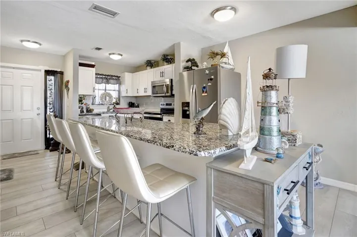 Kitchen with white cabinetry, a breakfast bar area, stainless steel appliances, light hardwood / wood-style floors, and stone countertops