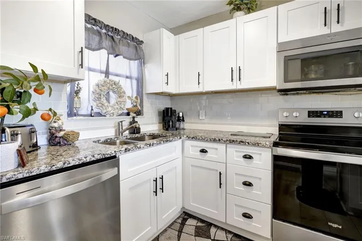 Kitchen featuring white cabinets, decorative backsplash, sink, light stone countertops, and appliances with stainless steel finishes