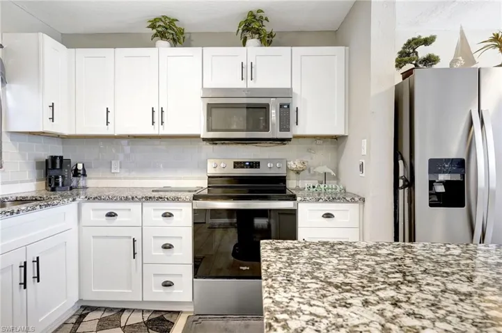 Kitchen featuring decorative backsplash, stainless steel appliances, white cabinetry, and light stone counters