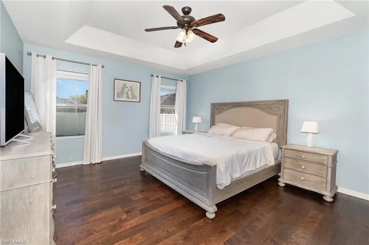 Bedroom with a ceiling fan, a tray ceiling, baseboards, and dark wood-type flooring