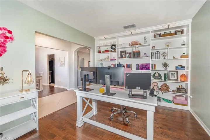 Office space featuring a textured ceiling, dark wood-style floors, baseboards, visible vents, and arched walkways
