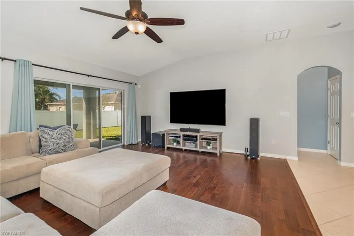 Living room with vaulted ceiling, wood finished floors, baseboards, arched walkways, and ceiling fan